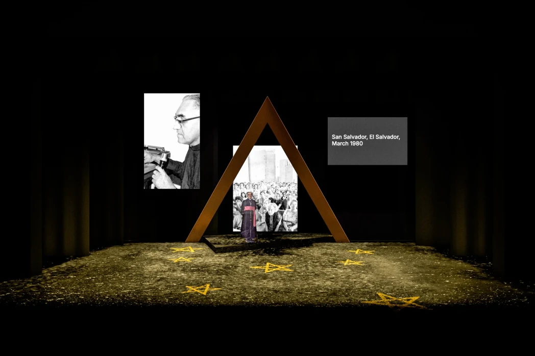 A stage with a triangular arch, a person in front, and two large photos. Yellow stars on the floor. Text reads 'San Salvador, March 1980.'