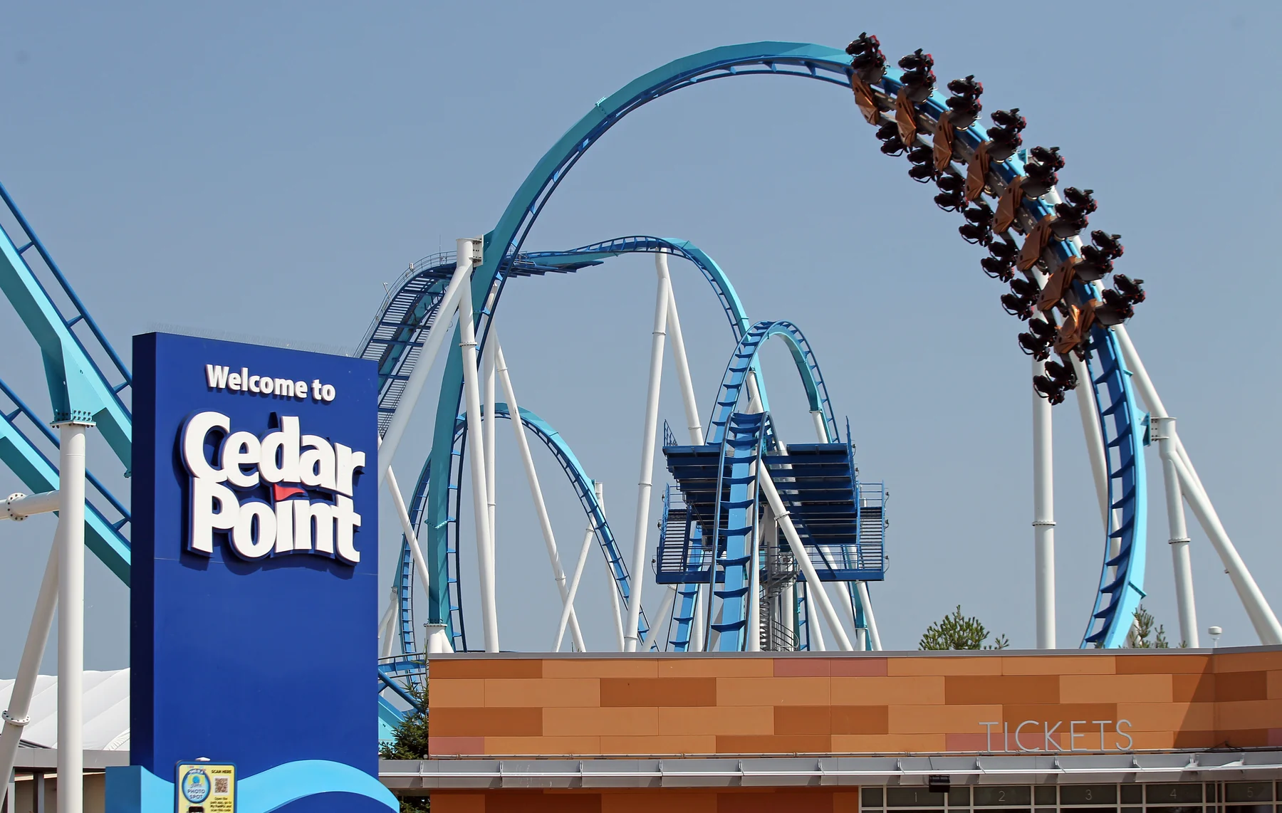 Roller coaster train cresting a loop on a blue track at Cedar Point against a clear sky.