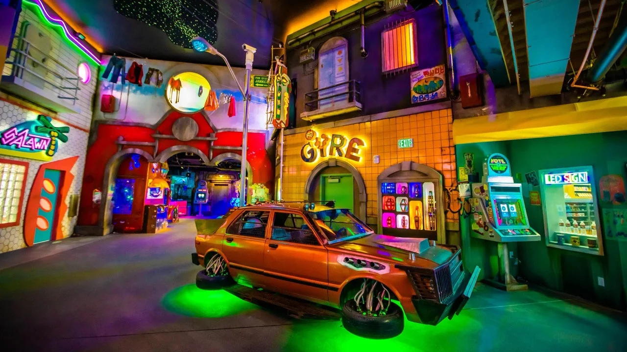 Neon-lit immersive street scene with glowing signage, themed storefronts, and a stylized orange car.