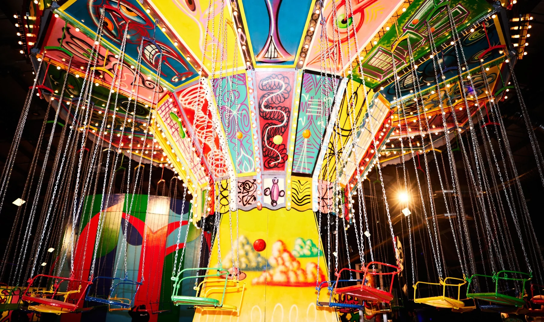 Colorful swing ride canopy with bright painted panels and suspended chairs in a carnival setting.