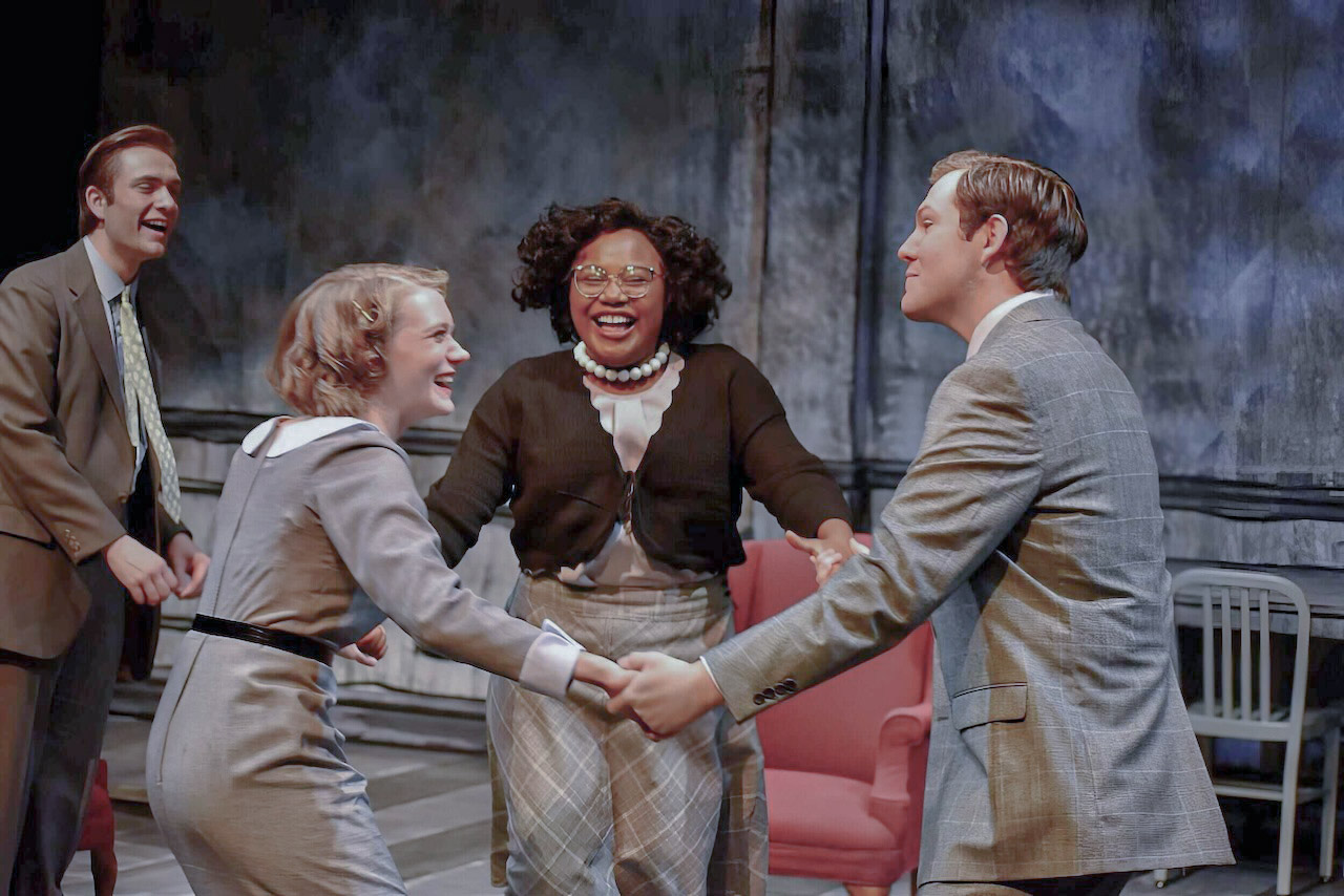 Performance image from An Enemy of the People showing the red furniture against the grayscale world, scenic design by Brandon PT Davis.