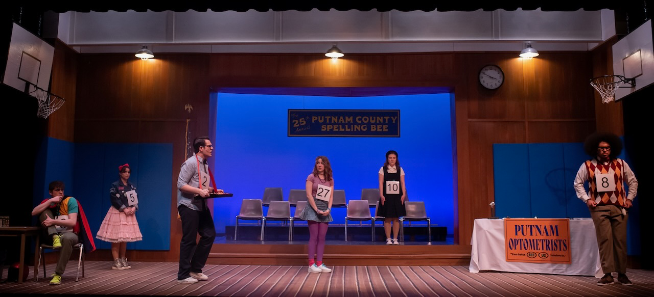 Scene from Putnam County Spelling Bee framed by the competition setup, scenic design by Brandon PT Davis.
