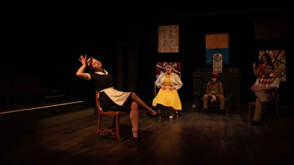 Production image from The Bald Soprano showing the fractured drawing-room world in performance, scenic and lighting design by Brandon PT Davis.